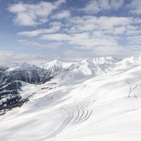 Breite schneebedeckte Berglandschaft unter bewölktem Himmel.