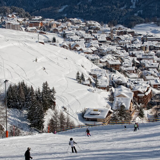 Blick auf ein verschneites Skigebiet mit Häusern im Tal.