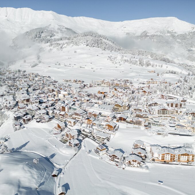 Luftbild eines verschneiten Bergdorfs in winterlicher Landschaft.