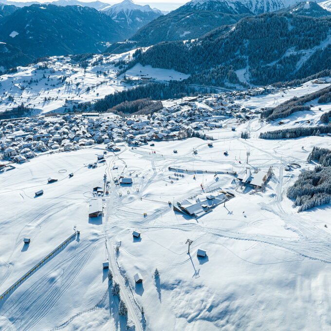 Luftaufnahme eines verschneiten Dorfes in den Alpen.