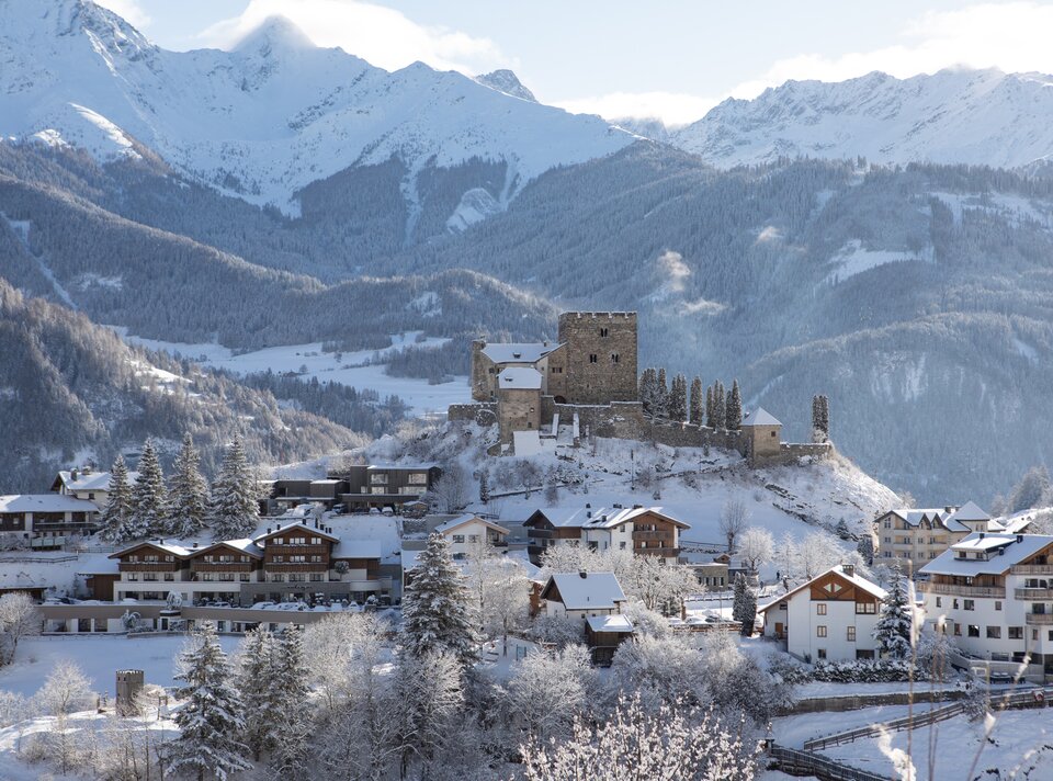 Sneeuwbedekt landschap met een kasteel en bergen op de achtergrond.
