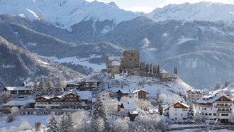 Sneeuwbedekt landschap met een kasteel en bergen op de achtergrond.