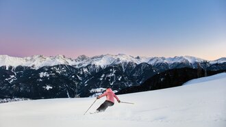 A skier in a pink jacket skiing against a stunning mountain backdrop.