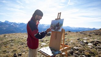 An artist stands in the mountains painting a landscape.
