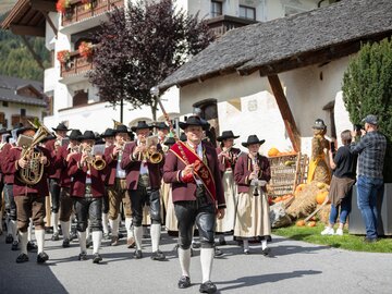 Eine Musikkapelle zieht durch eine bergige Ortschaft in traditioneller Tracht.