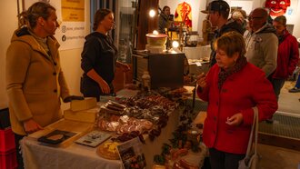 Bezoekers verkennen een kraam met kaas, worst en meer op een markt.