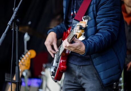 A guitarist playing a red electric guitar on stage.