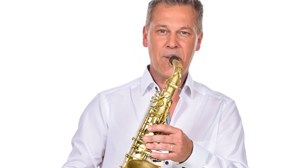 Ein Mann mit goldenem Saxophon in einem weißen Hemd, er lächelt.