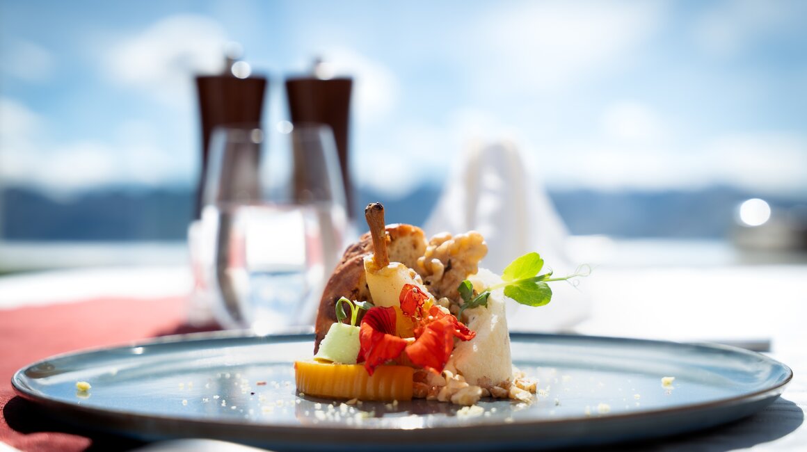 Ein kunstvoll angerichtetes Dessert mit Obst und essbaren Blüten, serviert in einer eleganten Umgebung.