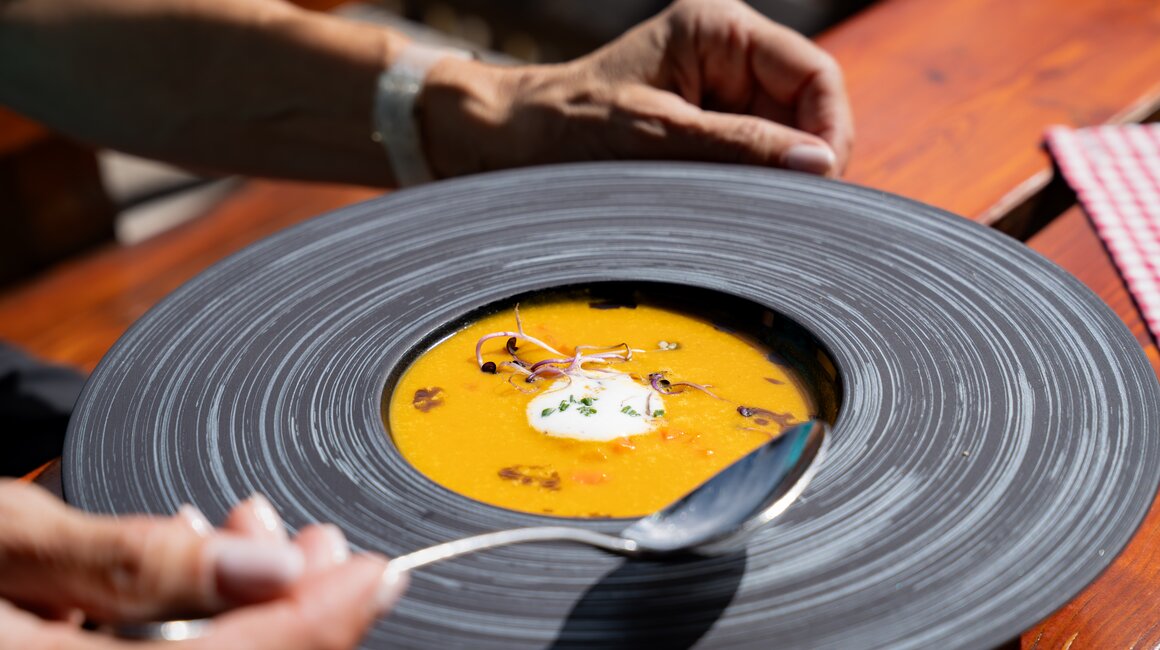 Ein Teller mit gelber Suppe, Sahne und Sprossen wird serviert.