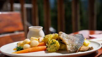 Ein Teller mit gegrilltem Fisch, Kartoffeln und buntem Gemüse.