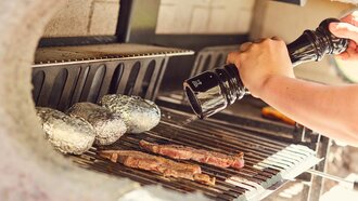 Ein Grill mit Rindersteaks und Folienkartoffeln, gewürzt.