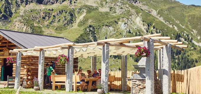Außenansicht einer Almhütte mit Gästen in den Bergen.