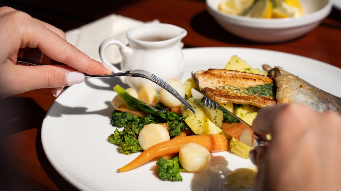 Detailaufnahme eines gefüllten Tellers mit Fisch und frischem Gemüse.