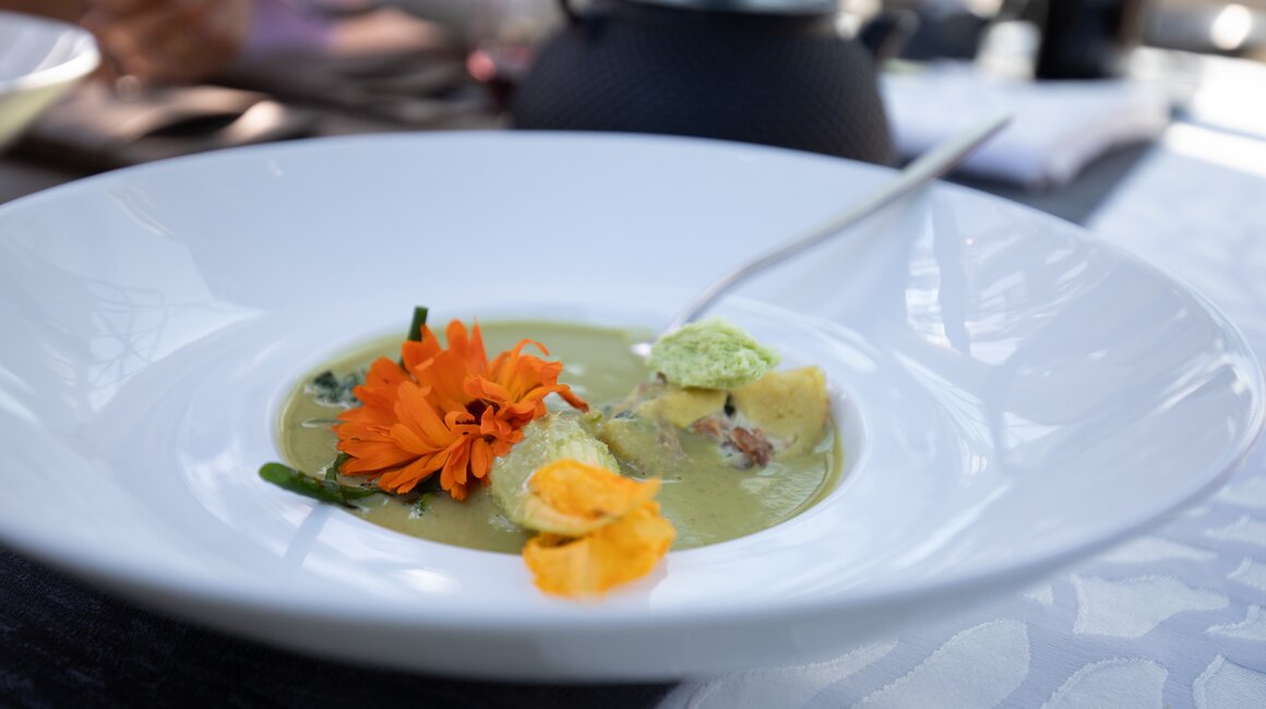 Ein Teller mit grüner Suppe, dekoriert mit essbaren Blüten und Kräutern.