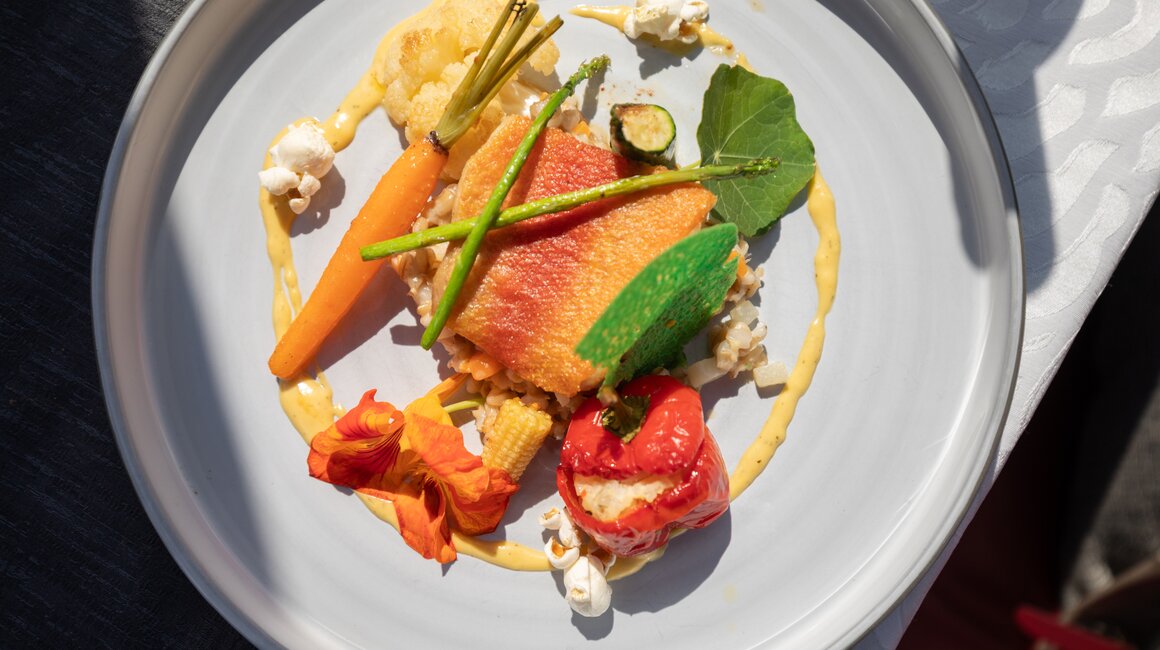 Ein kunstvoll angerichtetes Gericht mit Fisch und buntem Gemüse.