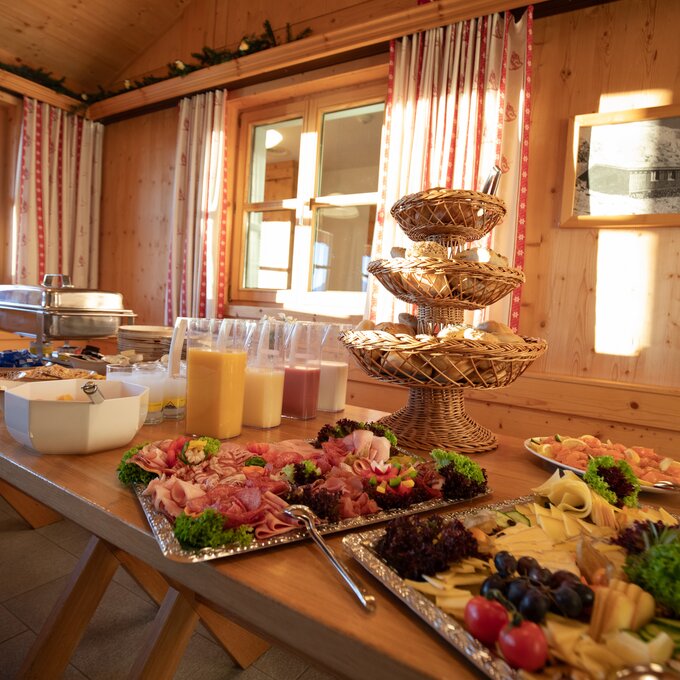 Ein Buffet mit Wurst, Käse, Salat und Getränken in einem Holzraum.