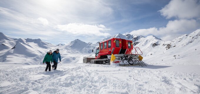 Two people walking in the snow near a red snowcat.