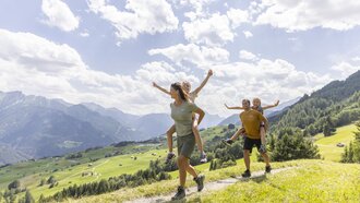 Eine Familie wandert auf einem Bergweg mit strahlendem Himmel.