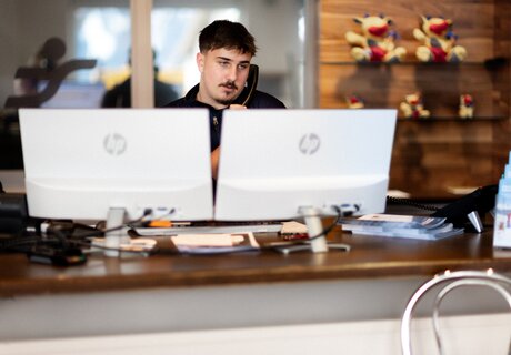 Ein Mitarbeiter spricht am Telefon an einem Schreibtisch mit zwei Monitoren.