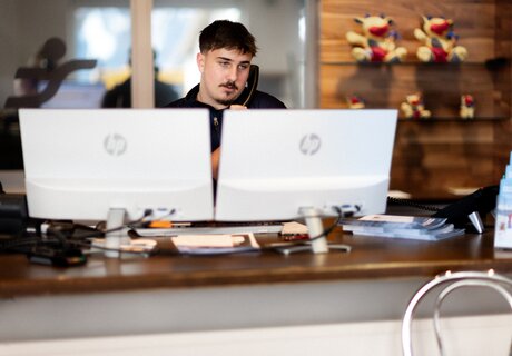 Ein Mitarbeiter spricht am Telefon an einem Schreibtisch mit zwei Monitoren.