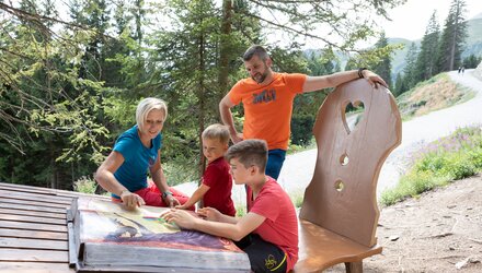 Family exploring a large book outdoors on a wooden bench.