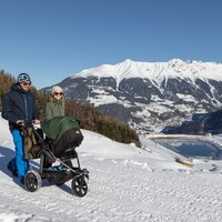 Couple with stroller on a snowy path in the mountains.