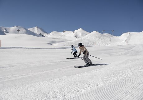 Two skiers on a snowy slope under a clear blue sky.