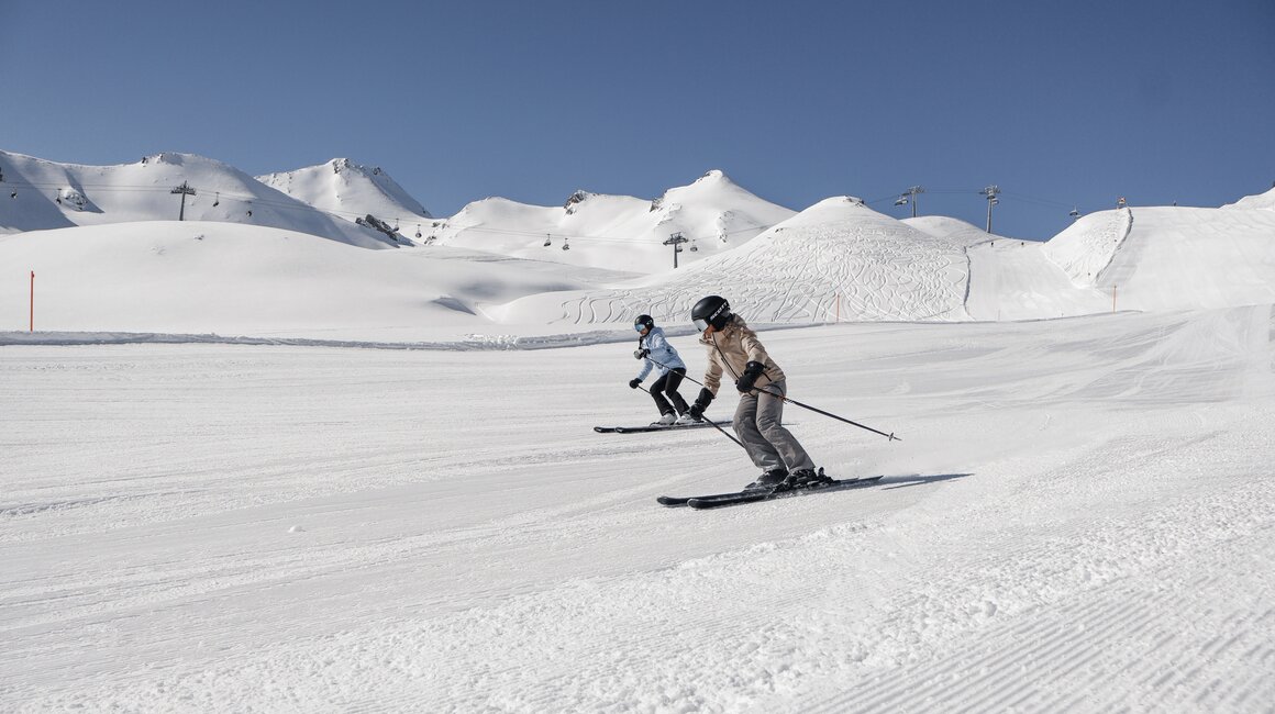 Twee skiërs op een besneeuwde helling onder een heldere blauwe lucht.