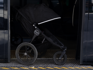 A black stroller is positioned at a subway door.