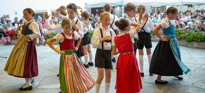 Children dancing in traditional attire on a stage.