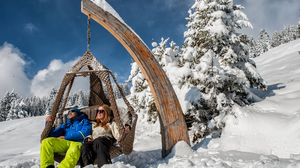 A couple relaxing in a hanging chair in a snowy winter landscape.