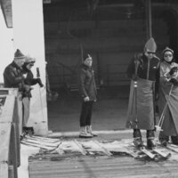 Fünf Personen in Winterkleidung und Skiausrüstung warten am Lift.