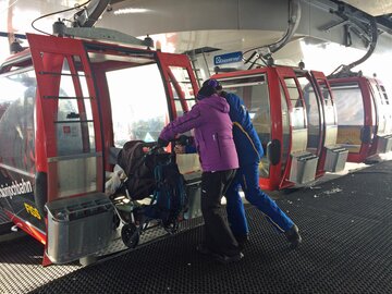 A couple assists boarding a gondola with a stroller.