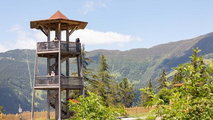 Wooden lookout tower surrounded by mountains and trees.