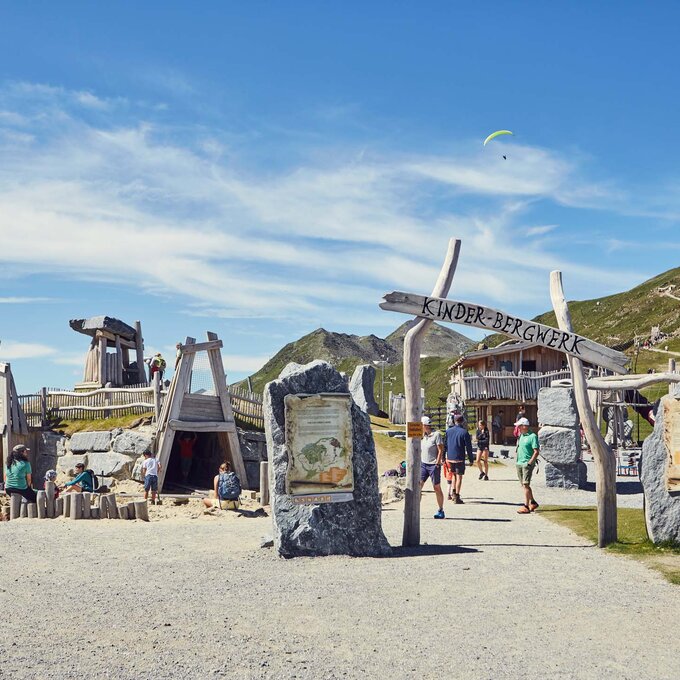 Ein kinderfreundlicher Bergspielplatz mit Holzstrukturen und Wanderern.