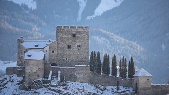 Ein Blick auf eine Burg in den Alpen, umgeben von Schnee und Tannen.