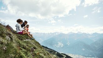 Drei Personen sitzen auf einem Berg und genießen die Aussicht auf die Alpen.