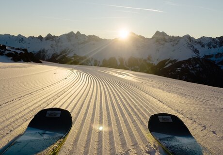 Ansicht auf frisch präparierte Piste mit Ski und Sonnenaufgang.