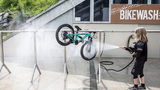 Ein Kind reinigt ein Mountainbike mit einem Hochdruckreiniger.