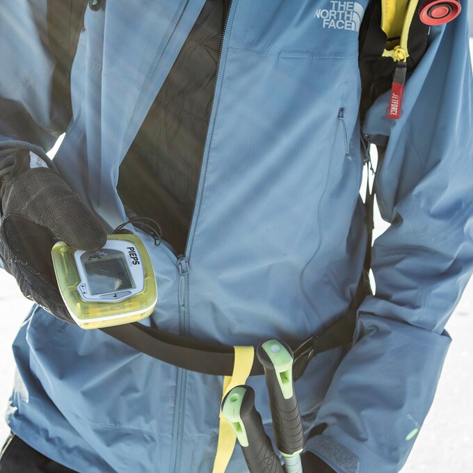 Person trägt Bergsteigerjacke und hält ein GPS-Gerät in der Hand.