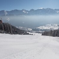 Blick auf eine schneebedeckte Piste mit Bergpanorama.