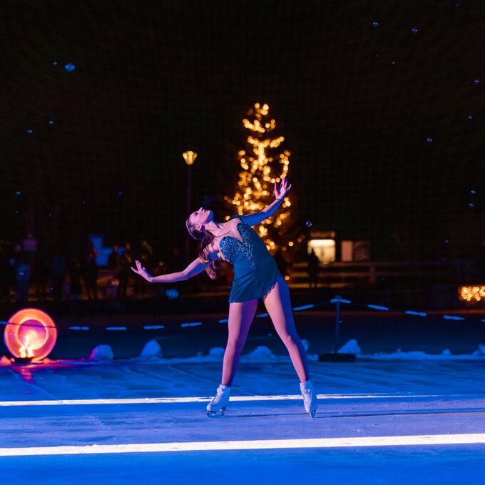 Eiskunstläuferin führt während einer Aufführung bei Nacht auf einer Eisbahn vor festlicher Kulisse auf.