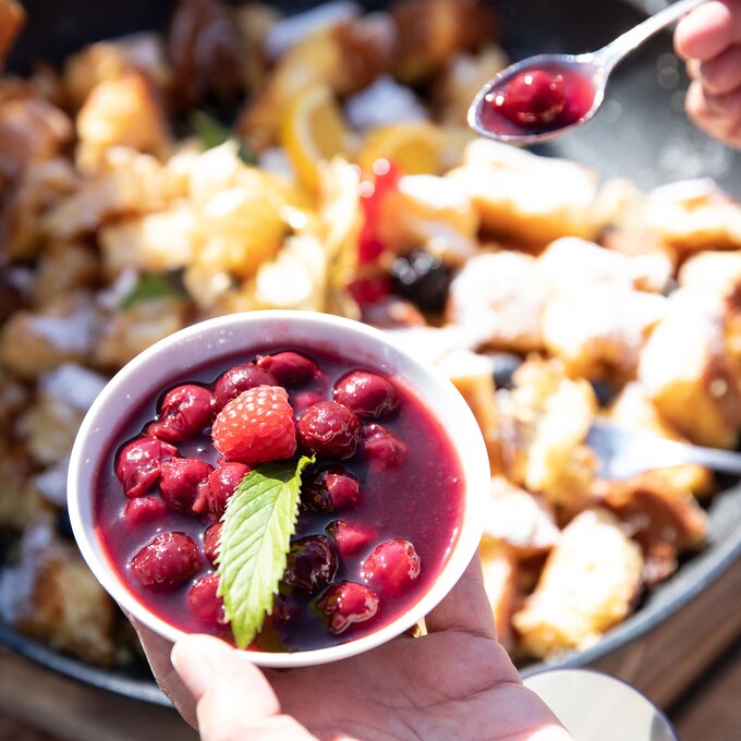 Eine Schale mit roten Beeren, serviert mit Minze und anderen Speisen im Hintergrund.