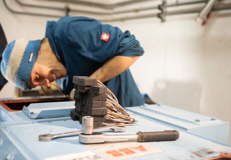 A technician works on a machine with tools and cables.