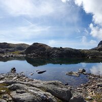 Ein stiller Bergsee spiegelt den Himmel in den Alpen.