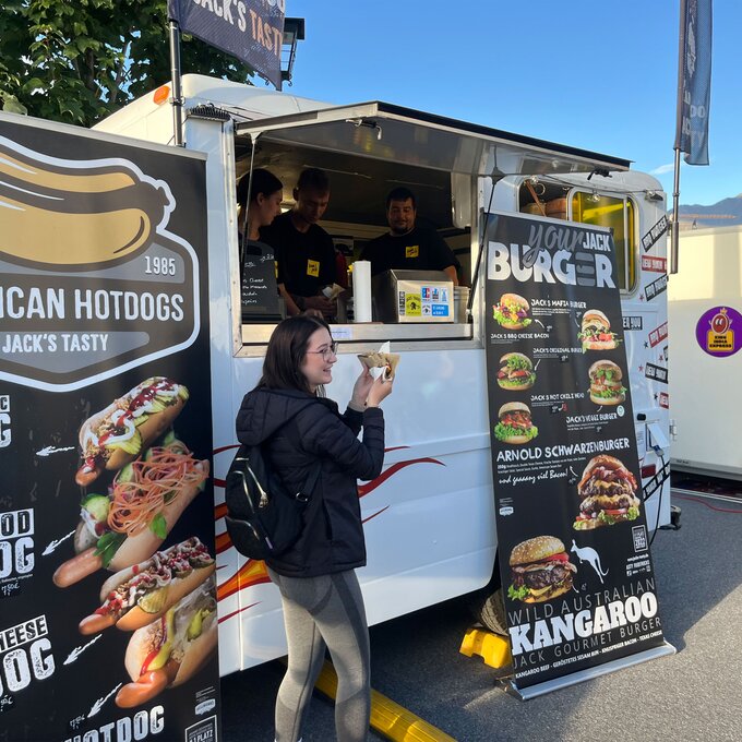 Ein Imbisswagen Angebote Hotdogs und Burger, während ein Kunde isst.