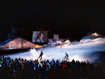 The image depicts a stunning nighttime snow event featuring bikers and lights.