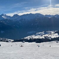 Schneebedeckte Landschaft mit Bergen und Skifahrern im Hintergrund.