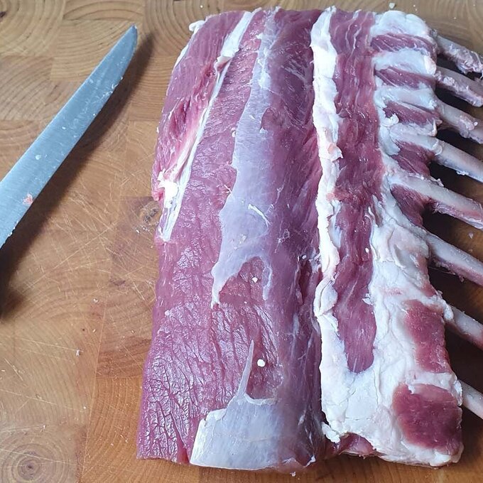 Rohes Rippchen liegt auf einem Holzbrett neben einem Messer.